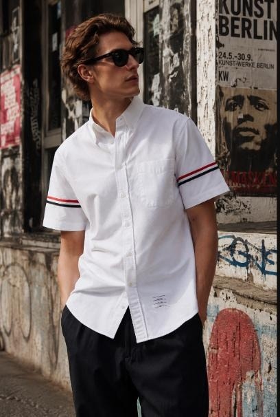 Man in white short-sleeve Oxford shirt with red-and-navy armband stripe, black trousers, Berlin street art backdrop