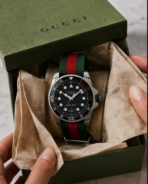 Gucci Dive watch with green-red-green striped strap displayed inside its signature green box