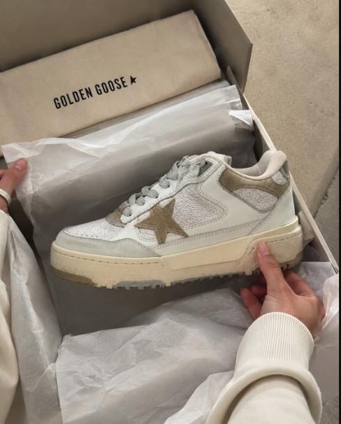 Cream and olive Golden Goose star-logo sneaker being lifted from its dust-bag-lined box