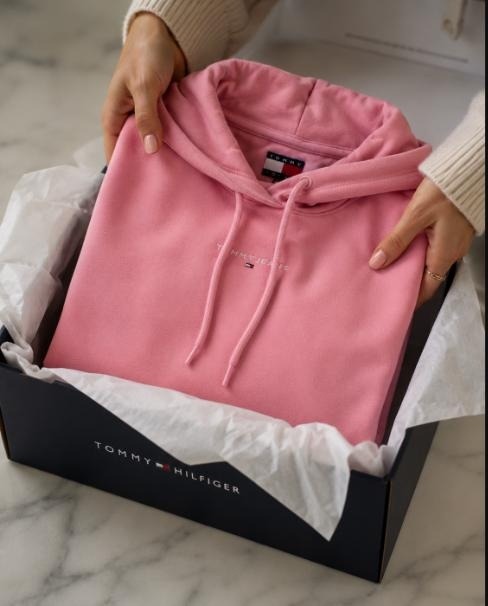 Pink Tommy Hilfiger logo hoodie being lifted from its navy signature packaging box